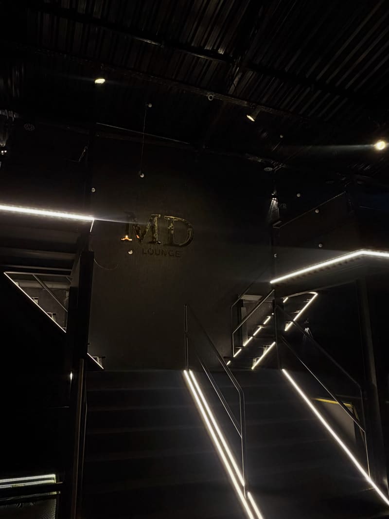 Letreiro MD Lounge no interior, com escada e corrimão em iluminação linear